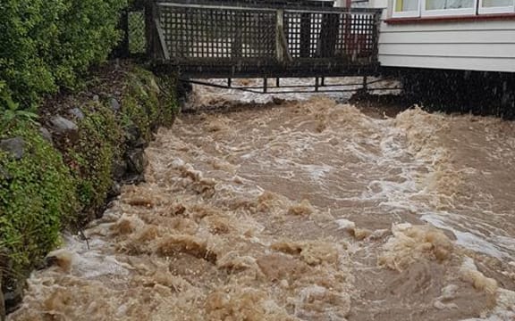 A flooded stream runs past a house in Akaroa