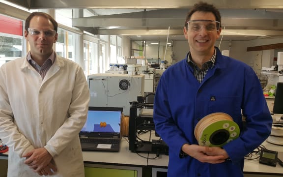 Marc Gaugler and Florian Graichen in front of 3D printing machines in the lab at Scion. Florian is holding a roll of wood-based bioplastic that can be used in the printers.