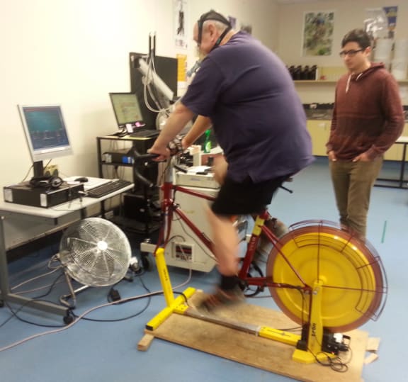 A photo of Colin Daley on an exercise bike with PhD student Adam Lucero