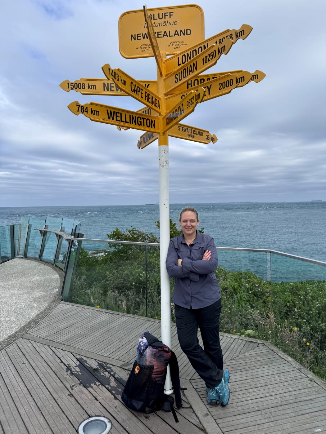 Journalist and author Naomi Arnold standing in front of the signposts at Bluff, the start of Te Araroa trail