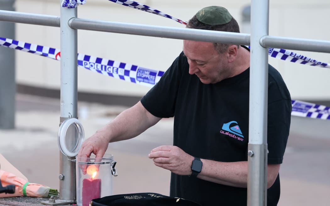 A member of the Jewish community lights a candle at the scene of a shooting at Bondi Beach in Sydney on December 15, 2025. Two gunmen who shot and killed 15 people at a Jewish celebration on Sydney's iconic Bondi Beach were a 50-year-old father and his 24-year-old son, Australian police said. (Photo by DAVID GRAY / AFP)