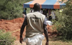 An officer of the Directorate of Criminal Investigations (DCI) walks at the mass-grave site in Shakahola, outside the coastal town of Malindi, on April 25, 2023. The death toll in an investigation linked to a Kenyan cult that practised starvation has climbed to 201, as investigators on May 13, 2023 unearthed 22 more bodies from a coastal forest, a government official said. (Photo by Yasuyoshi Chiba / AFP)