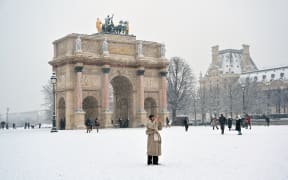 A pedestrian takes a picture near the Arc de Triomphe du Carrousel covered in snow in Paris on January 5, 2026. (Photo by Christophe DELATTRE / AFP)