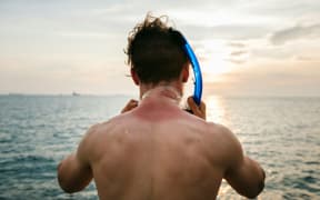 Man with sunburnt neck in the sea prepares to snorkel.