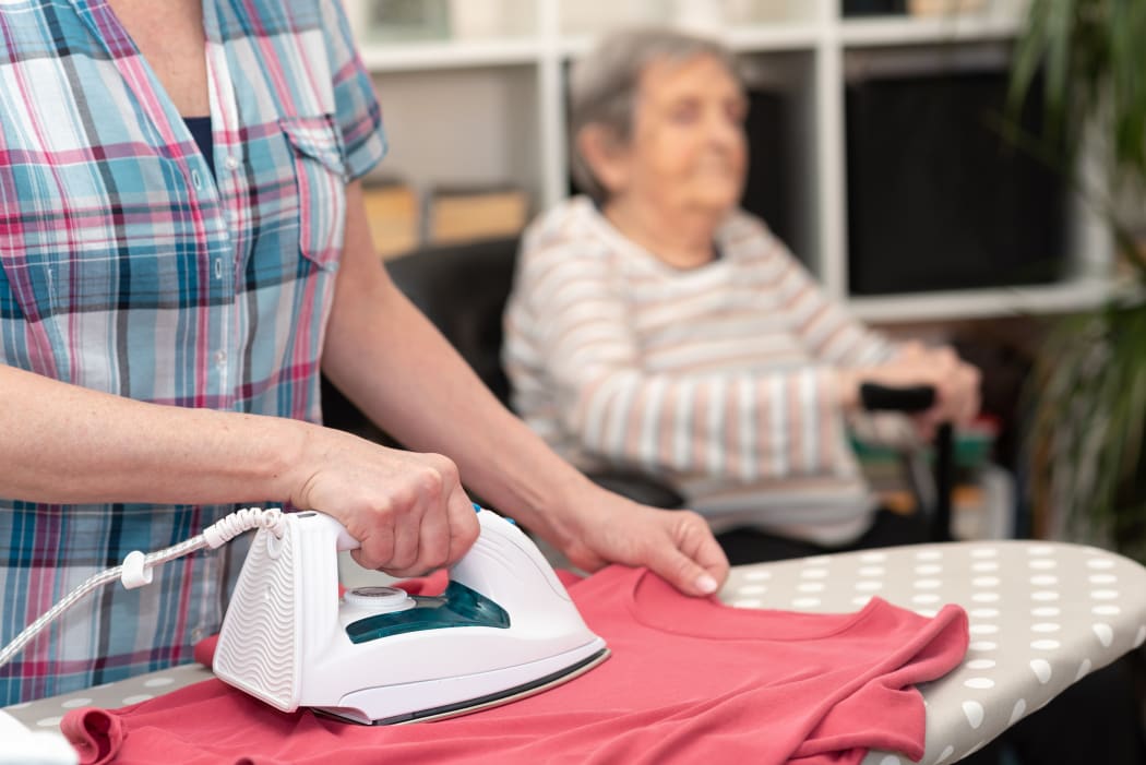 Home, helper ironing clothes for elderly woman.
