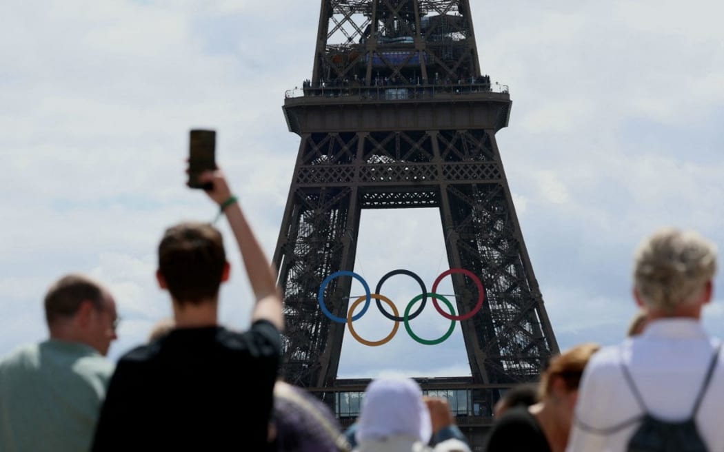 Visitors look at The Eiffel Tower adorned with The Olympic Rings ahead of the 2024 Olympic Games in Paris on July 16, 2024. (Photo by EMMANUEL DUNAND / AFP)