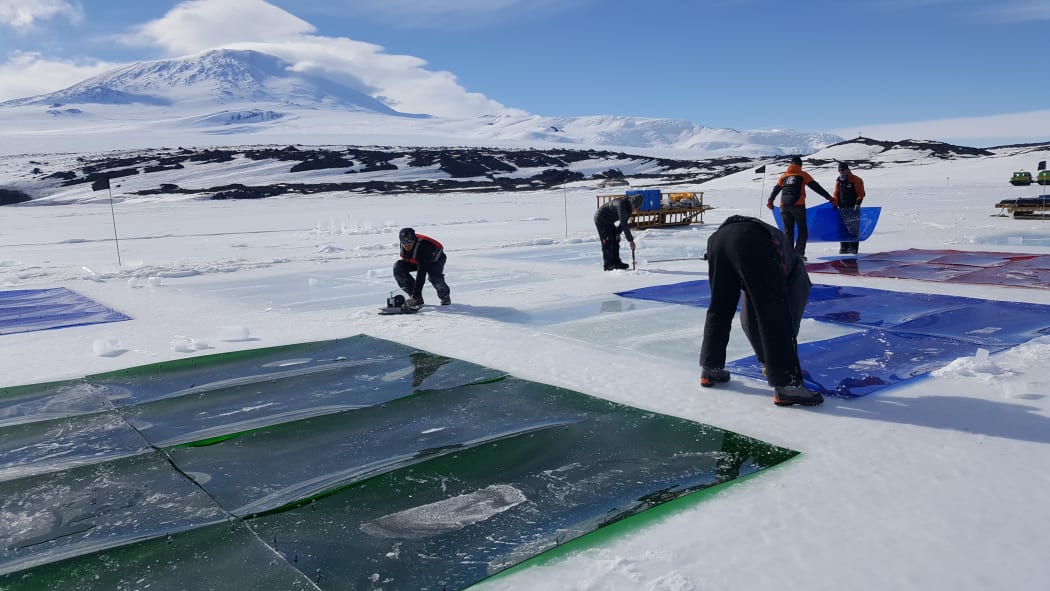 Researchers lifting coloured perspex panels used in an experiment on the algae that grows under the sea ice. Mt Erebus in the background.