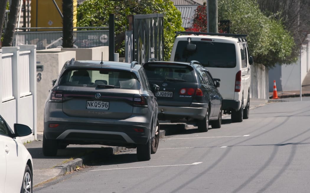 Pedestrians try to use the footpath in Auckland where cars are parking over the kerb.