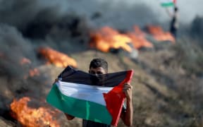 A Palestinian holds a flag during a protest against Israeli army raid in Jenin, along Israel-Gaza border fence east of Gaza City July 3, 2023. Israel has stepped up operations in the northern West Bank, home to Jenin city and its adjacent refugee camp, a stronghold of Palestinian armed groups where there has been a spate of attacks on Israelis as well as attacks by Jewish settlers on Palestinian communities. 
 (Photo by Majdi Fathi/NurPhoto) (Photo by MAJDI FATHI / NurPhoto / NurPhoto via AFP)