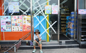 A woman sits outside a convenience store with windows taped up for protection on Lantau island in Hong Kong on September 1, 2023, hours before the expected arrival of Super Typhoon Saola. Hong Kong grounded flights, shut down its stock market and closed schools on September 1 as Super Typhoon Saola barrelled towards China's southern coast. (Photo by Peter PARKS / AFP)