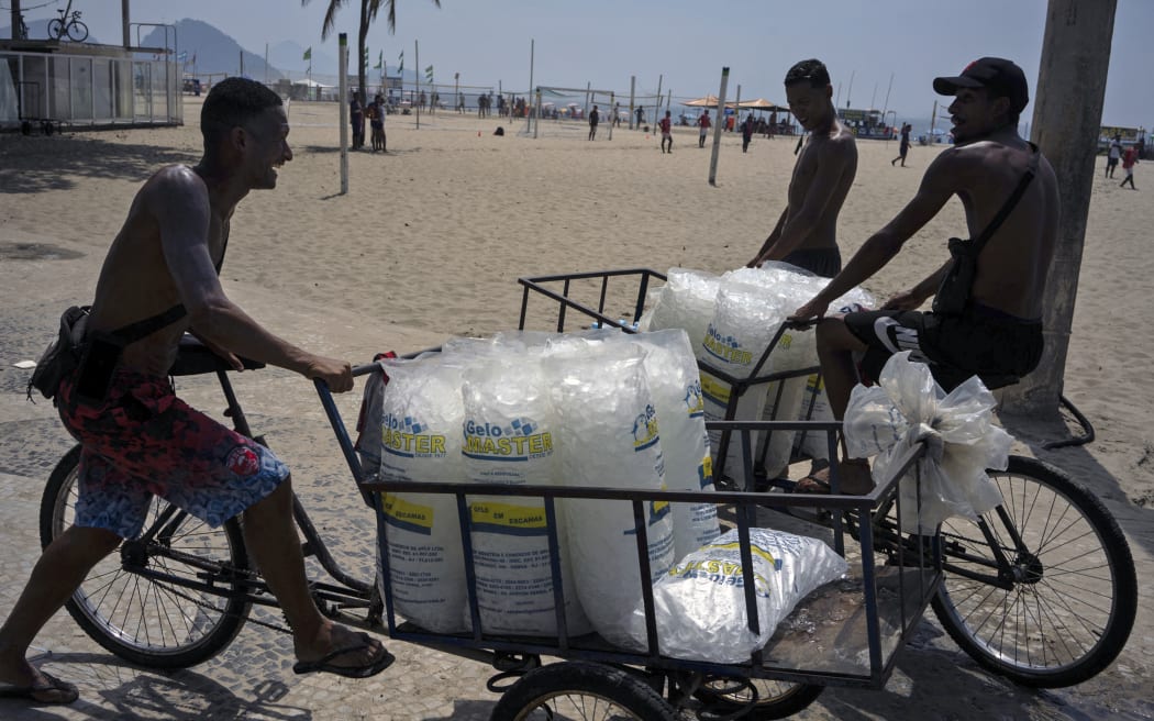 Street vendors offer bags of ice on Copacabana Beach during a heatwave in Rio de Janeiro, Brazil, on November 18, 2023. The heatwave that has been affecting much of Brazil for several days continues, with stifling temperatures in cities like Rio de Janeiro, where the heat index reached a record of 59.3 °C (138.7 degrees Fahrenheit), as reported by authorities. (Photo by Tercio TEIXEIRA / AFP)