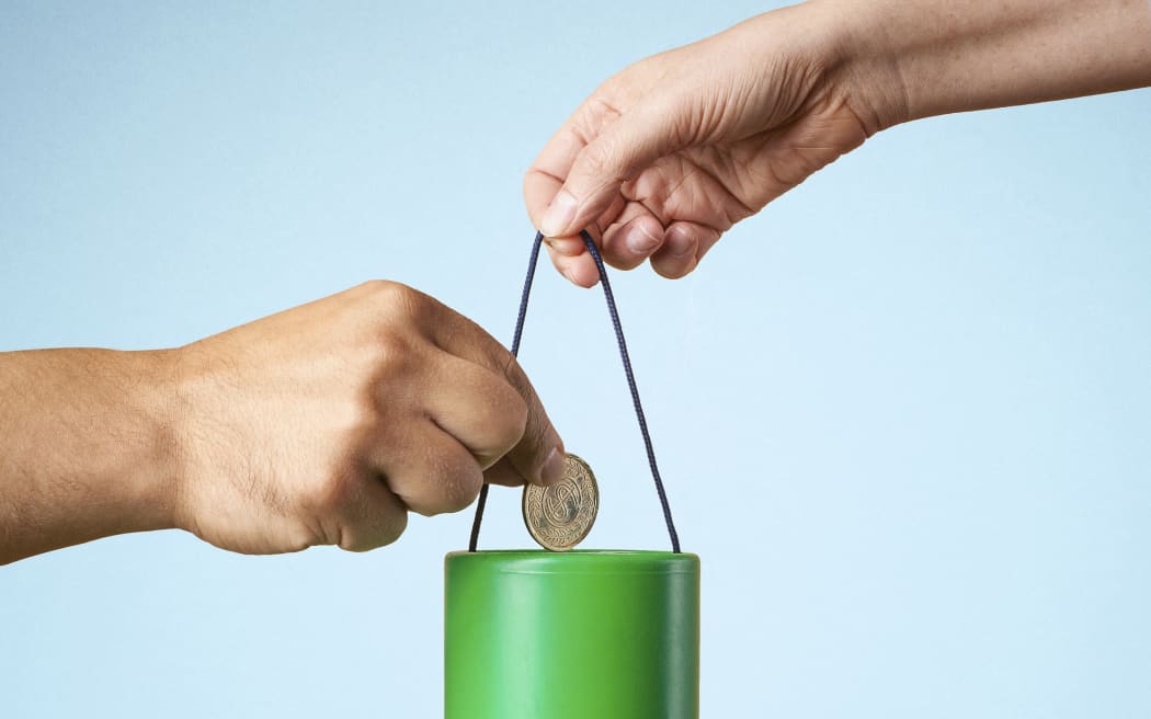 Studio shot of hand putting coin into charity collection box (Photo by Sverre Haugland / Cultura Creative / Cultura Creative via AFP)