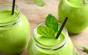 Jars of healthy green smoothie with fresh spinach on wooden table, closeup view