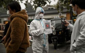 A health worker holds up a QR code to scan as people queue to test for Covid-19 at a swab collection station in Beijing on 20 November 2022.