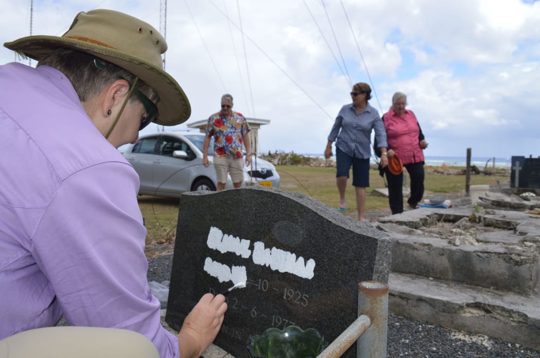 A volunteer repaints an engraved headstone with crumbling graves in the background