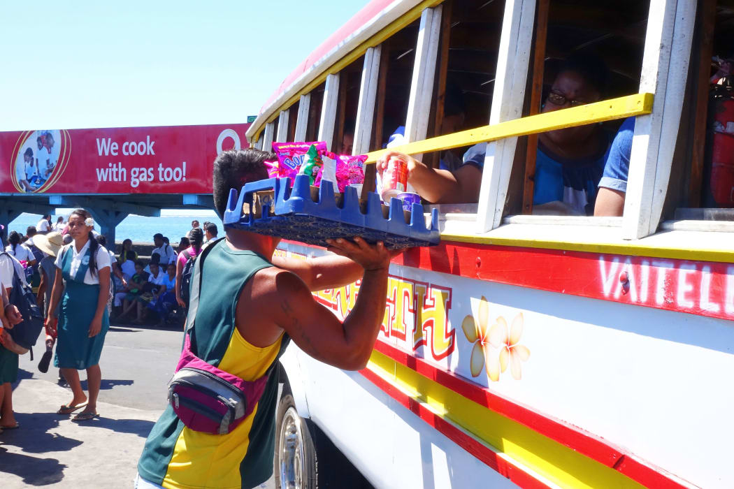 Street vendors at the Apia bus station can be seen winding in and out amongst the colorful Samoan buses selling food and drinks to passengers.