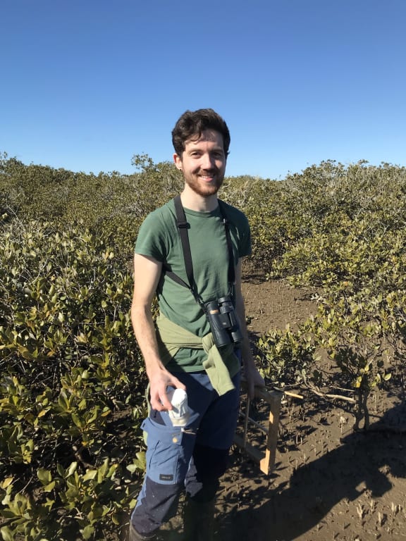 Jacques de Satge holds his banded rail footprint testing device & a small quadrat in front of some mangroves.