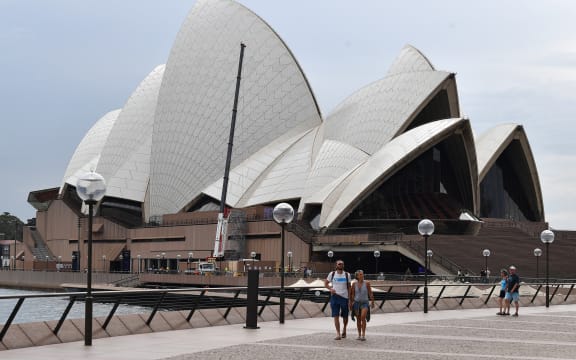 A few people walk along Circular Quay outside the Opera House in Sydney on March 25, 2020, as people stay away due to restrictions to stop the spread of the worldwide COVID-19 coronavirus outbreak.