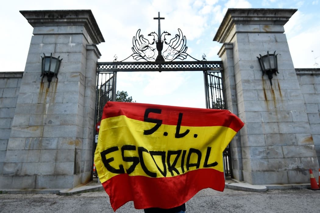 A man holds a Spanish flag in front of the closed access road to the Valle de los Caidos (The Valley of the Fallen), a monument to the Francoist combatants who died during the Spanish civil war and Franco's final resting place.
