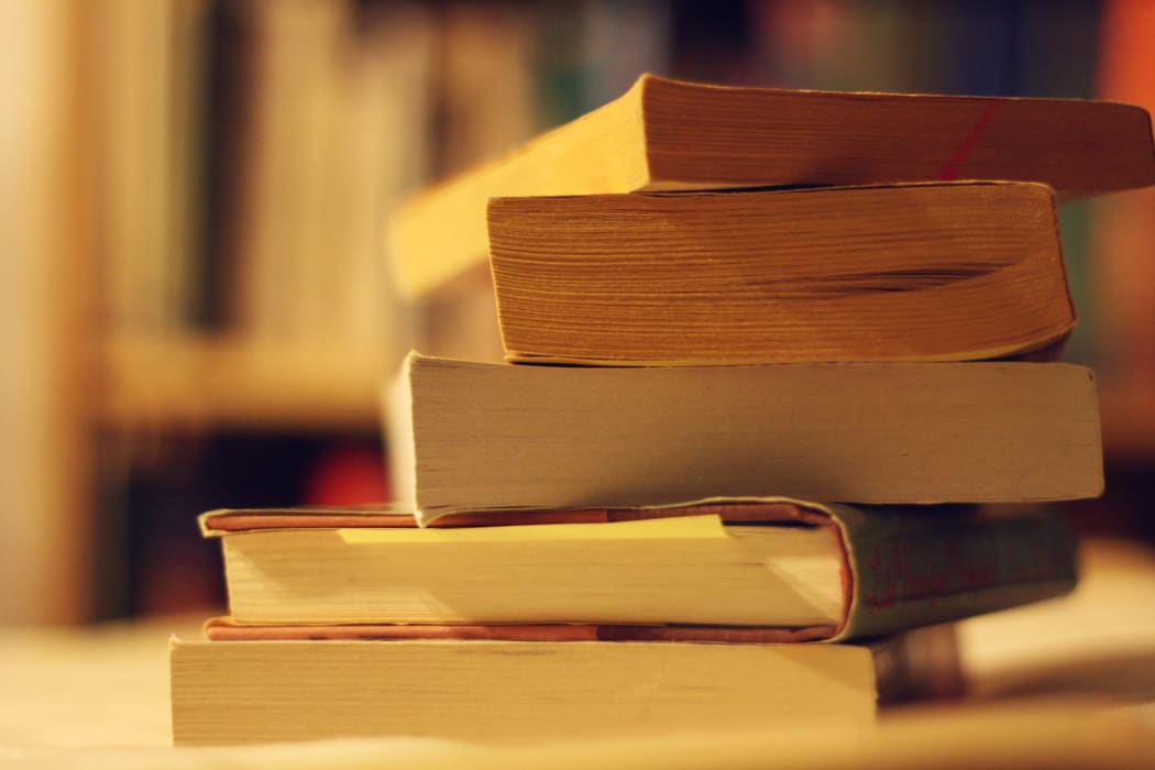 A stack of books with a bookshelf behind them.