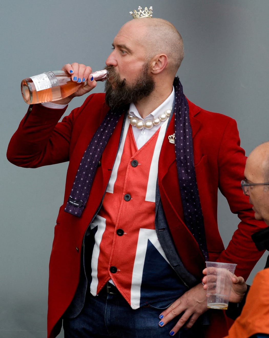 A person sporting a Union Jack waistcoat and wearing a small crown on his head, drinks following the Coronation Ceremony for King Charles III and Queen Camilla at Westminster Abbey in central London, on May 6, 2023. - The set-piece coronation is the first in Britain in 70 years, and only the second in history to be televised. Charles will be the 40th reigning monarch to be crowned at the central London church since King William I in 1066. Outside the UK, he is also king of 14 other Commonwealth countries, including Australia, Canada and New Zealand. (Photo by PIROSCHKA VAN DE WOUW / POOL / AFP)