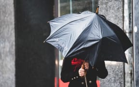 A woman has difficulty holding an umbrella from strong winds in rainy weather.