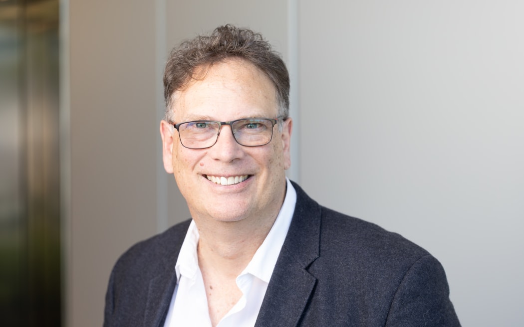 This is a head and shoulders shot of Paul looking to the camera. He is wearing glassesa white shirt with a casual blazer.
