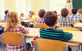 education, elementary school, learning and people concept - group of school kids sitting and listening to teacher in classroom from back
