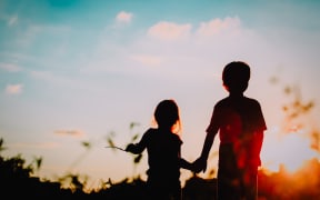 little boy and girl silhouettes holding hands at sunset nature