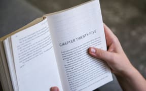 A young person holds a chapter book open as they read.