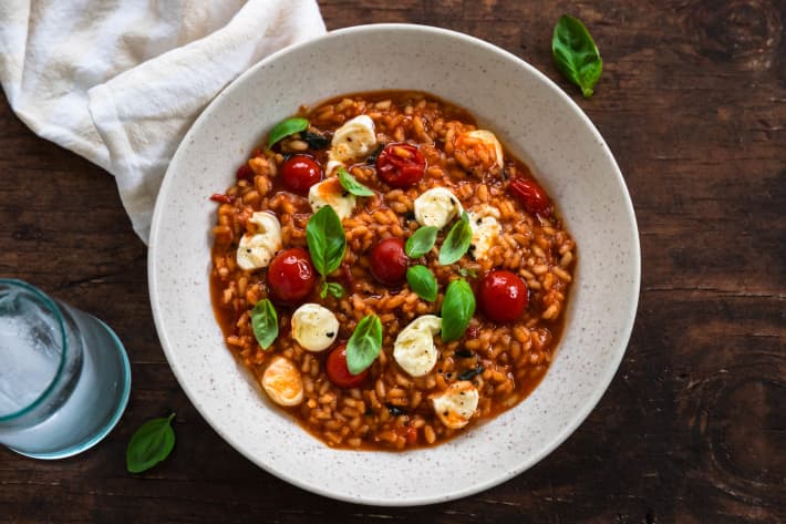 A bowl of Cherry tomato and mozzarella risotto decorated with basil leaves