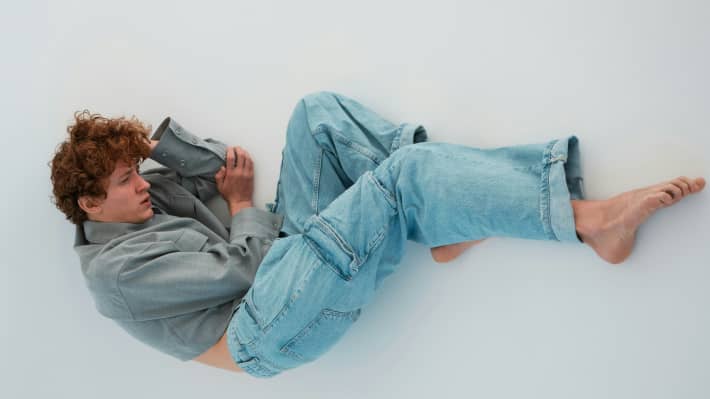 A redhead boy is barefoot and holds his head in his hands, looking worried.