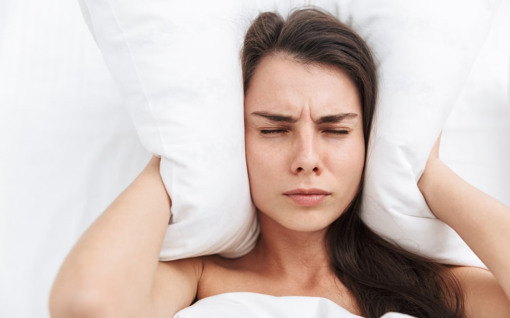 Top view close up of a beautiful young woman laying in bed, cover ears with a pillow