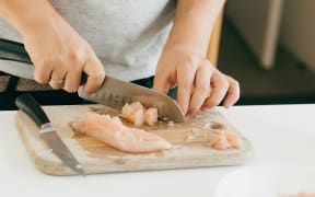 A person chopping chicken on a board in a kitchen.