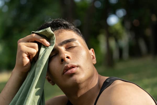 A man using a cloth to wipe his sweat outdoors on a hot summer day.
