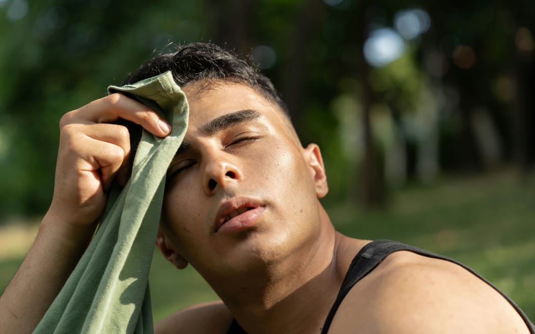 A man using a cloth to wipe his sweat outdoors on a hot summer day.