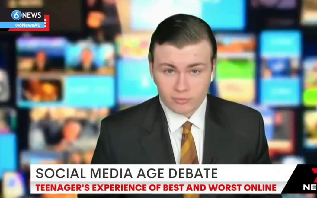 Leo is seated for a live interview with a green screen of a busy newsroom behind him. He wears a suit and has AirPods in to hear the presenter.