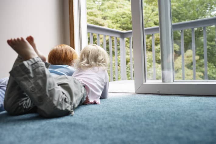 Sisters (3-6) lying on carpet looking through balcony door