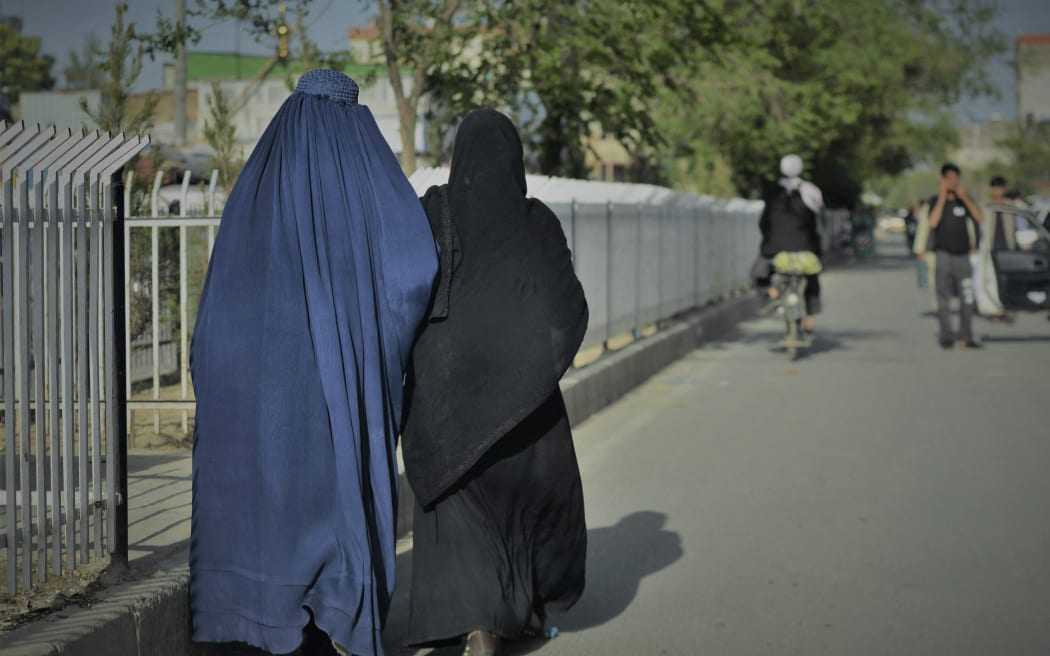 Women wearing a burqa (L) and a Niqab (R) walk along a street in Kabul on 7 May, 2022. - The Taliban on May 7 imposed some of the harshest restrictions on Afghanistan's women since they seized power, ordering them to cover fully in public, ideally with the traditional burqa.