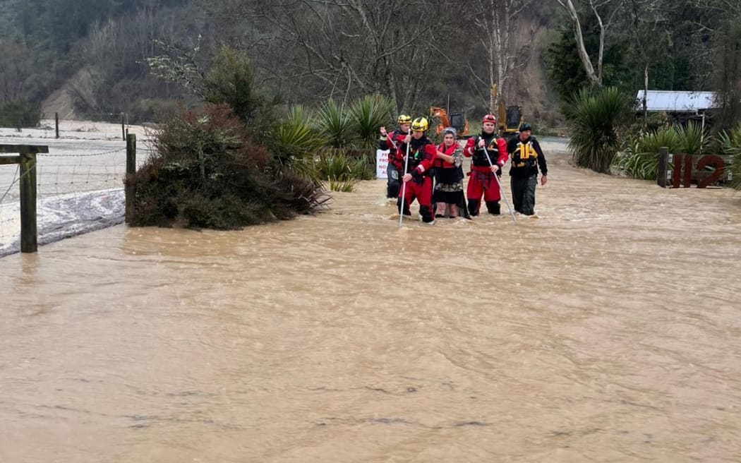 Two people are guided across dangerous floodwaters in Tasman on Friday 11 July, 2025, by members from Fire and Emergency NZ's specialist water response teams from Christchurch and Nelson, using long poles to test what lies under the water.