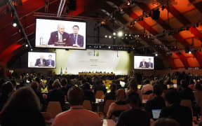 Delegates listen to French Foreign Minister Laurent Fabius speaking (on screens) during a plenary a session at the COP21 United Nations climate change conference in Le Bourget, outside Paris, on December 9, 2015.