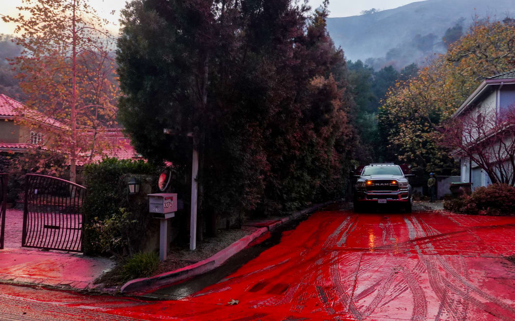 Foscheck fire retardant covers the road and nearby properties after being dropped by aircraft to slow the wildfire spread in Pacific Palisades, Los Angeles, California, on January 11, 2025, as wildfires continue in Los Angeles County. (Photo by Jason Ryan/NurPhoto) (Photo by Jason Ryan / NurPhoto / NurPhoto via AFP)