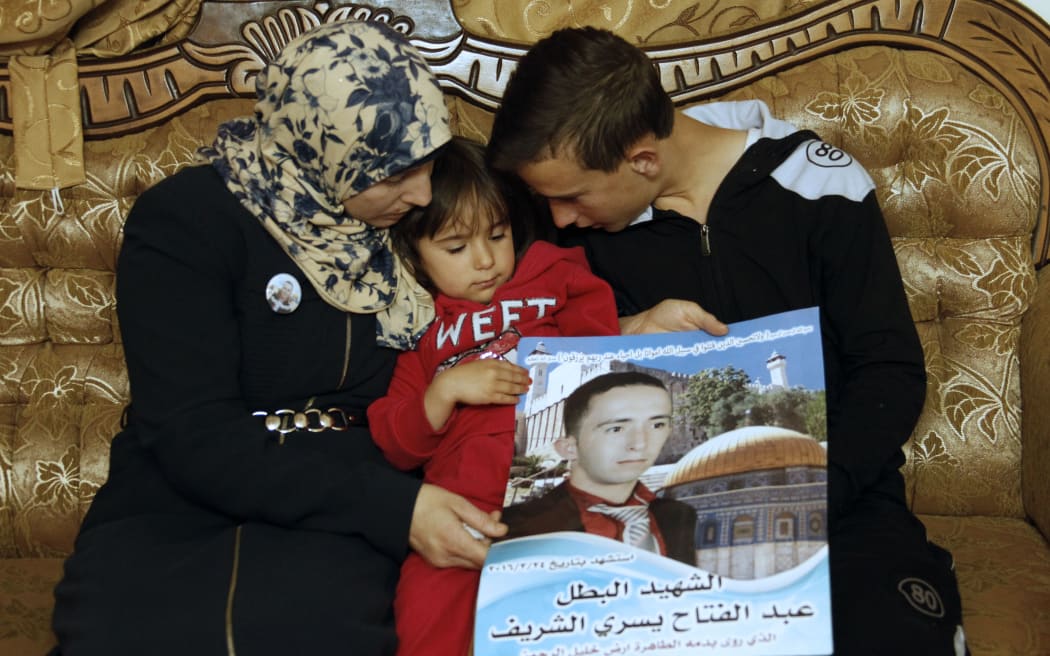 The mother and siblings of Palestinian Abdul Fatah al-Sharif, who was shot dead by Israeli soldier Elor Azaria, hold a poster breaing his portrait in the Israeli occupied West Bank city of Hebron.
