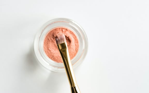 Makeup brush in container of pink eyeshadow