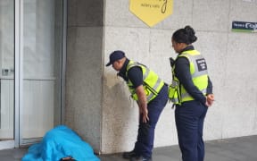 Auckland Council patrollers try to wake up a rough sleeper.