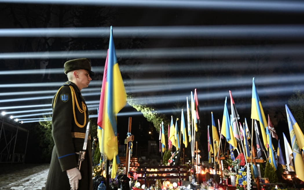A Ukrainian honour guard stands as a symbolic illumination called "Rays of Memory" is seen over the graves of Ukrainian soldiers, who died in the war with Russia, at Lychakiv Military Cemetery in Lviv on February 23, 2025, on the eve of the third anniversary of Russia's invasion of Ukraine.
