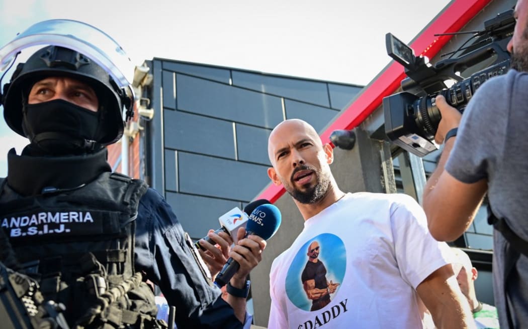 Andrew Tate (C), speaks to journalists as he is brought in for questioning by the Romanian gendarmes after a ten-hour long raid by police at their residency in Bucharest on August 21, 2024. Romanian authorities on August 21, 2024 searched the home of controversial influencer Andrew Tate, who is awaiting trial over human trafficking and rape charges, as part of a new investigation, officials said.
One of the world's best-known influencers known for misogynist and sometimes violent maxims, Andrew Tate has been accused of having formed an organised criminal network in early 2021 in Romania and Britain, along with his brother Tristan. They have denied the charges. (Photo by Daniel MIHAILESCU / AFP)