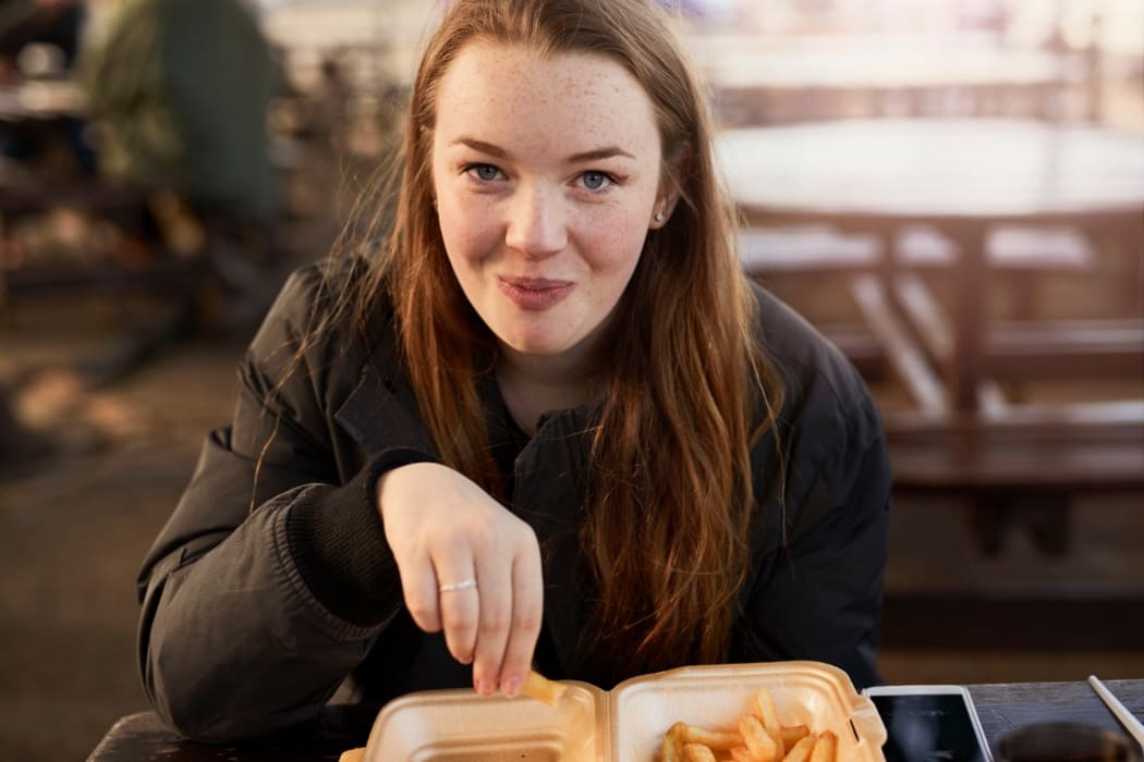 Portrait of young woman, outdoors, eating chips, Bristol, UK