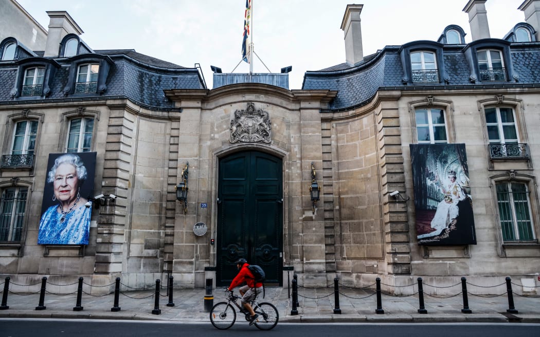 A cyclist rides as the Union Jack with the Royal Coat or Arms flies at half mast at the main gate of the British embassy in Paris and two portraits of Queen Elisabeth II hang on its walls after the annoucement of her death on September 9, 2022.