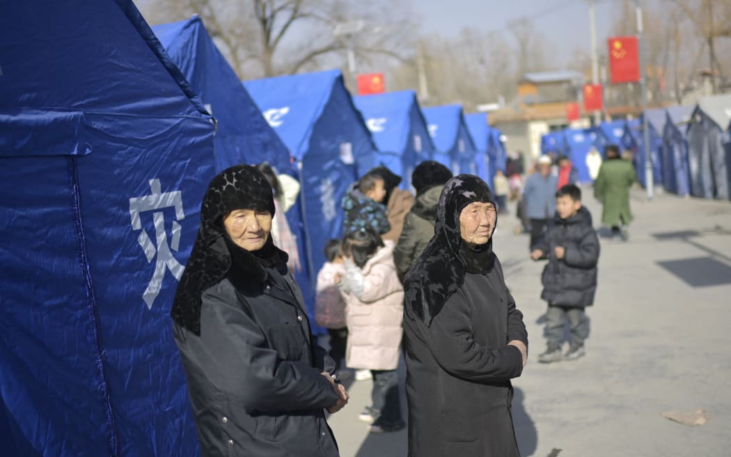 Earthquake-affected residents look on beside aid tents erected in a school compound at Gaoli village in Jishishan County in northwest China's Gansu province on December 20, 2023. Survivors of China's deadliest earthquake in years huddled in aid tents on Wednesday after overnight temperatures plunged well below zero, with the death toll rising to 131. (Photo by PEDRO PARDO / AFP)
